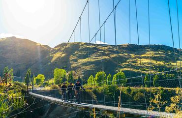 Cyclists on suspension bridge with green hills beyond