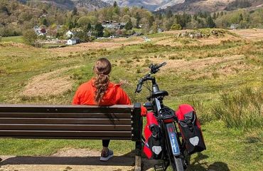Person sitting on bench with bike leaning on it looking out to green views