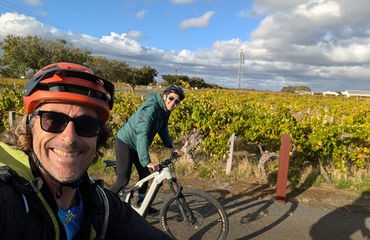 Two cyclists smiling at camera with vineyard in background