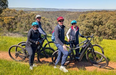 Four cyclists on green hill posing with bikes for photo
