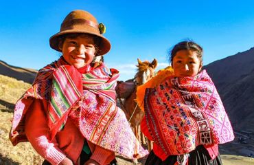 Two children in Peru wearing brightly coloured clothes and smiling at camera