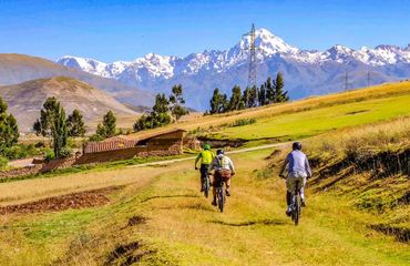 Cyclists riding on grassy path with snow capped mountains ahead