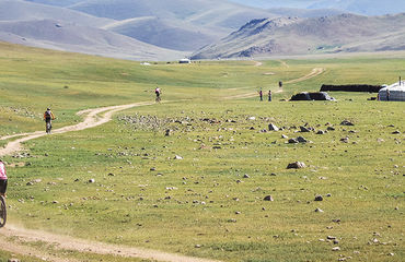 Cyclists riding along dirt track with yurts in background