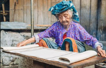 Older woman in colourful clothing with low table and paper spread out