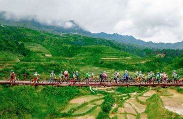 Lots of cyclists on a bridge with a mountain background
