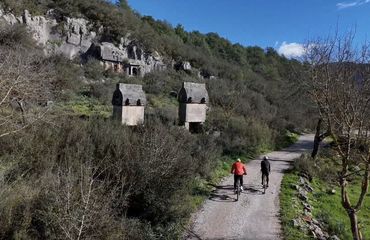 Cyclists riding a gravel road with abandoned buildings at the side