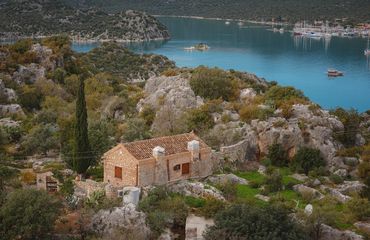 Old house on the hill with trees around and light blue sea beyond