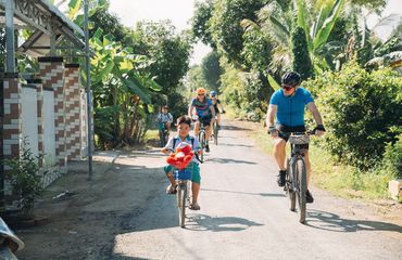 Cyclists - both adults and children on paved road with greenery all around