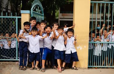 Lots of school children waving at camera and doing peace sign