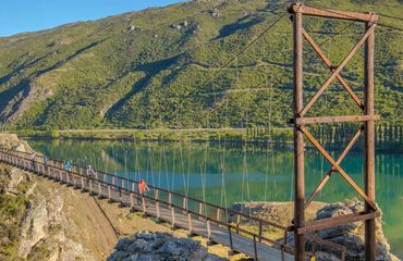 Cyclists riding over suspension bridge with blue green scenery