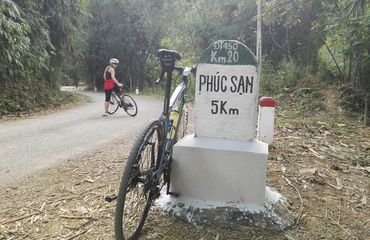 Bike resting against kilometre marker with person waiting in background