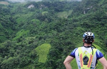 Cyclist with back to camera, looking down on green fertile hillside