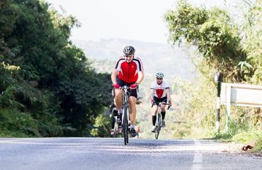 Cyclists riding up hill with green scenery