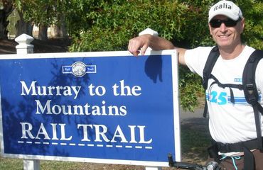 Man standing at 'Murray to the Mountains Rail Trail' sign