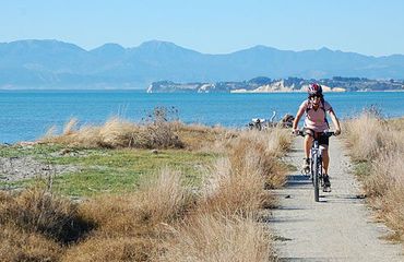 Cyclist riding along a grass lined path with sea and mountains behind