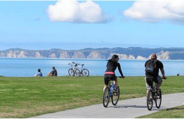 Cyclists on flat path with sea and cliffs in background