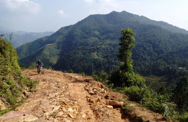 Cyclist riding up dirt track with mountains in background