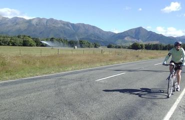 Cyclist riding along flat road with mountainous backdrop