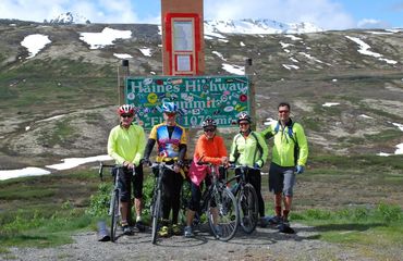 Group of cyclists posing by Haines summit sign