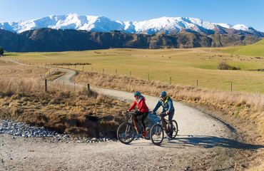 Cyclists on trail with snow capped mountains behind